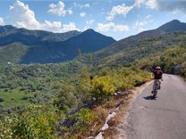 A cyclist riding a mountain road above a green valley